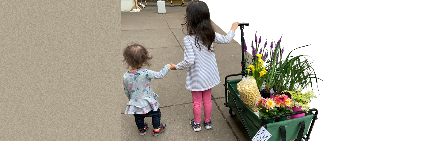 Two little children pulling a wagon full of colorful plants
