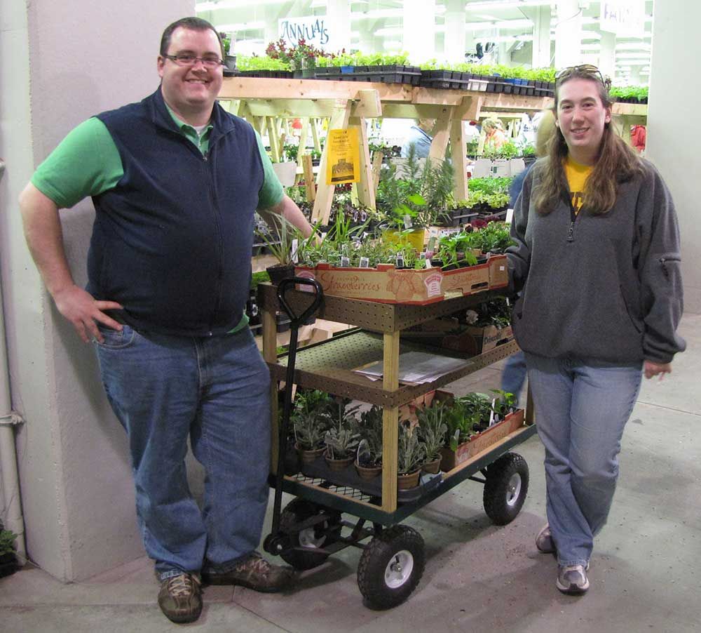 A flat garden cart with wooden shelf structure built above to hold plants