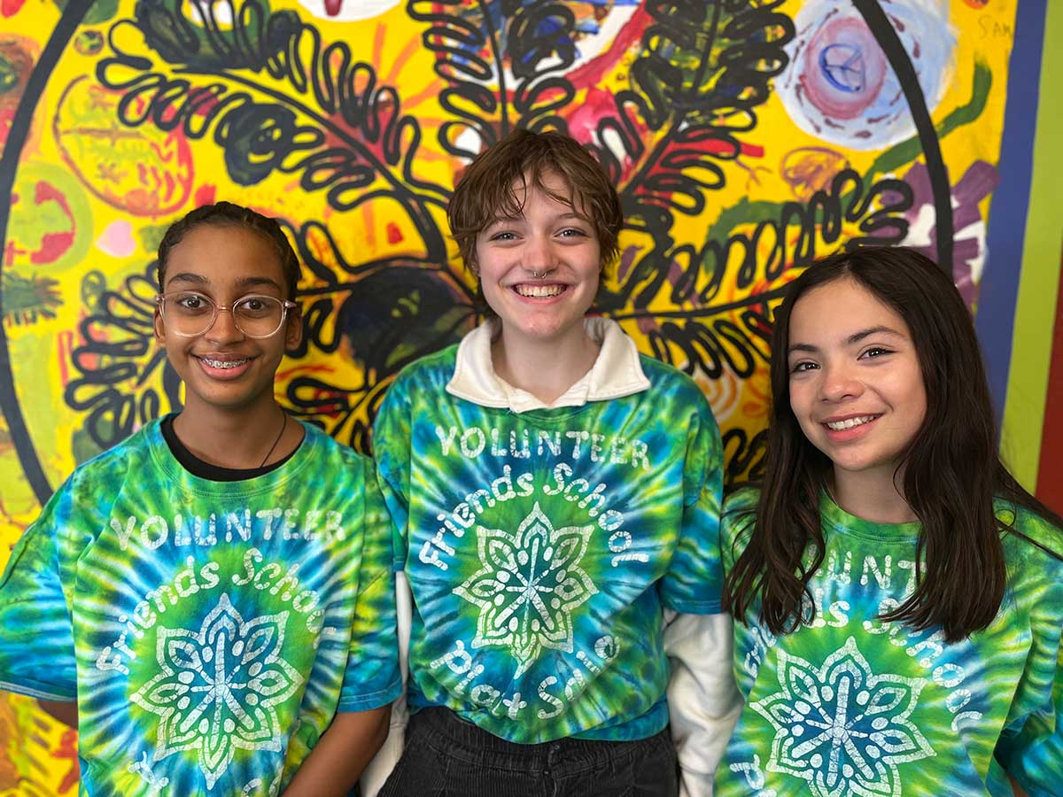 Three middle-school-aged students in blue-green tie-dyed t-shirts that say Friends School Plant Sale