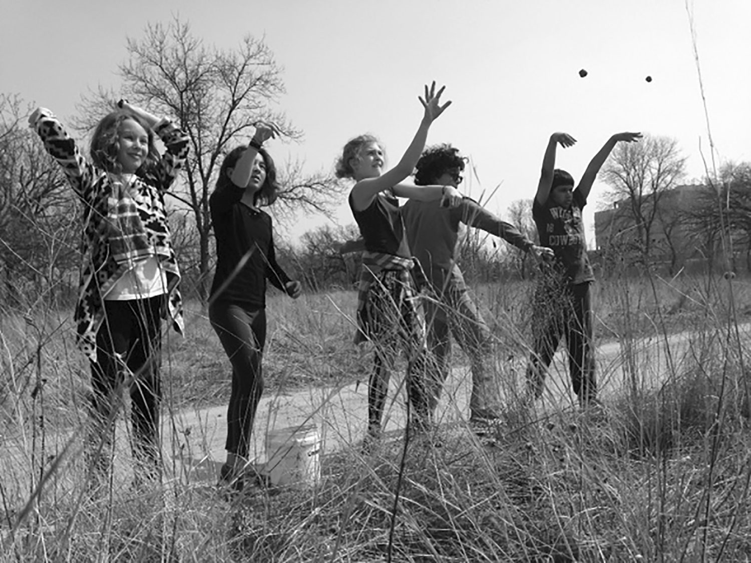 Five middle school students throwing something in a grassland