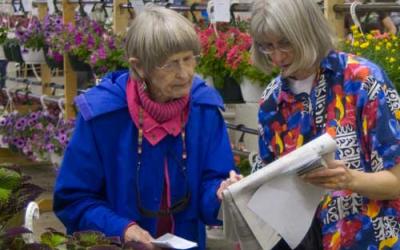 Two white women shopping for plants, looking at a catalog.