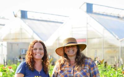 Two women smiling in front of greenhouses