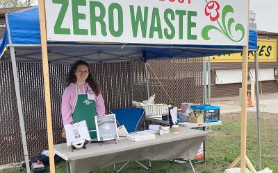 Volunteer standing at a table under a banner that reads Find out about ZERO WASTE